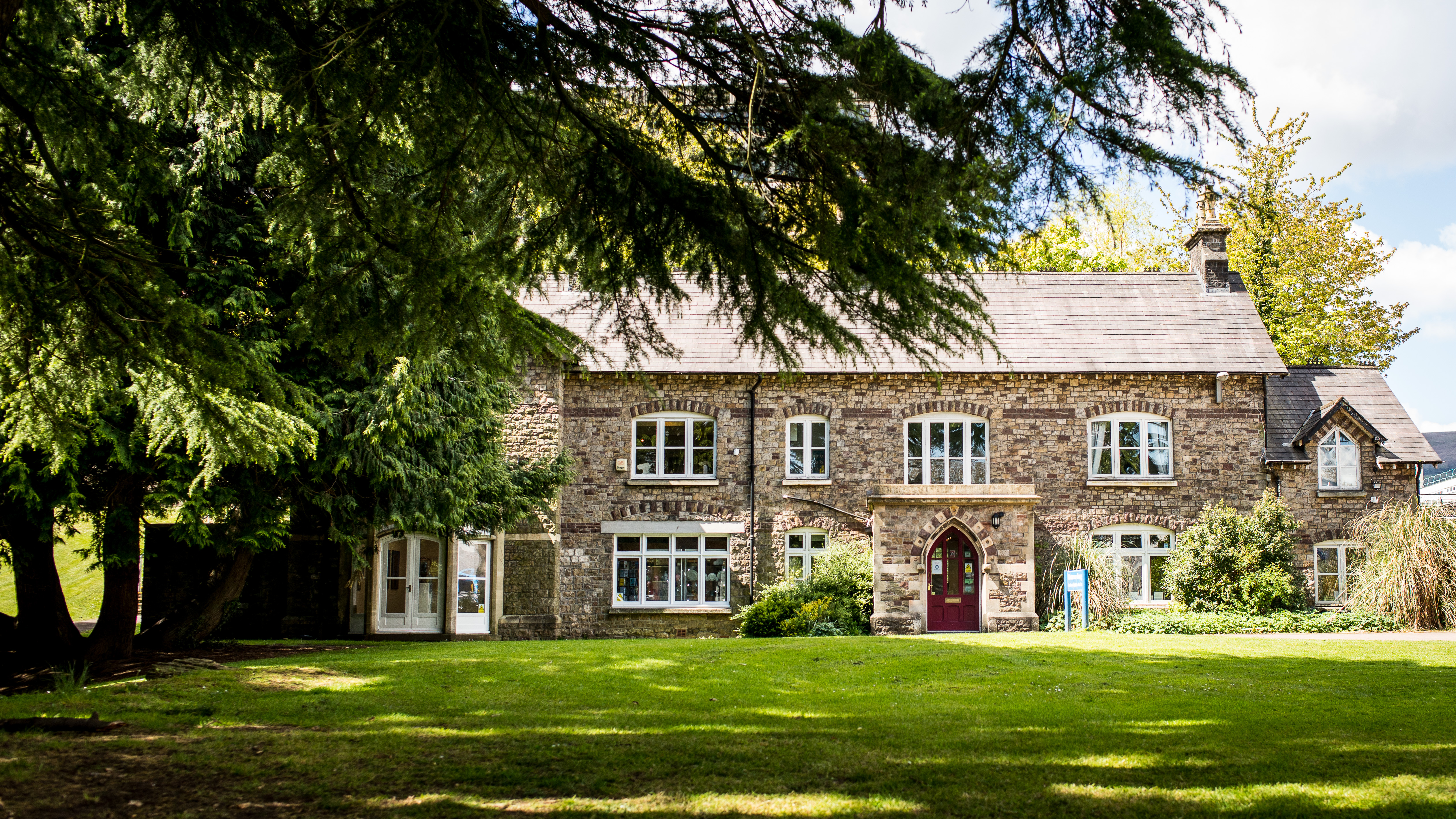 An outside view of Llantarnam Grange, a three story Victorian building, surrounded by grass and trees in Cwmbran