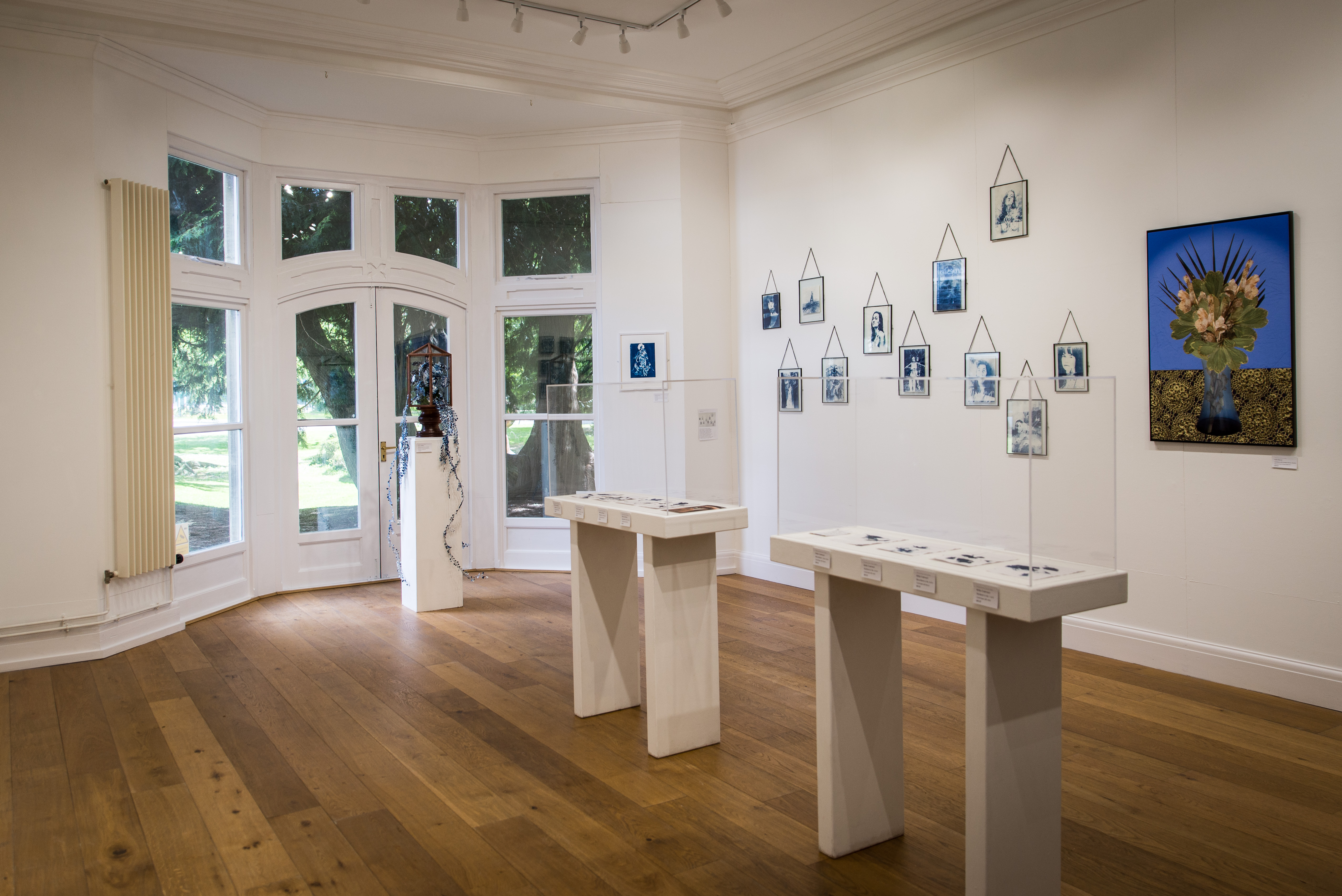 A view of Gallery 1, a big open rectangle room, white walls and a high ceiling. There are floor to ceiling bay windows at the end of the room, with lots of natural light.