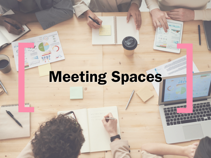 A faded background of an overhead desk shot, over which text reads 'Meeting Spaces' in between the Creative Cardiff Brackets in Pink