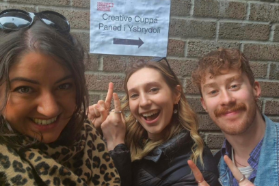 The Creative Cardiff team pointing at a sign that says 'Creative Cuppa'